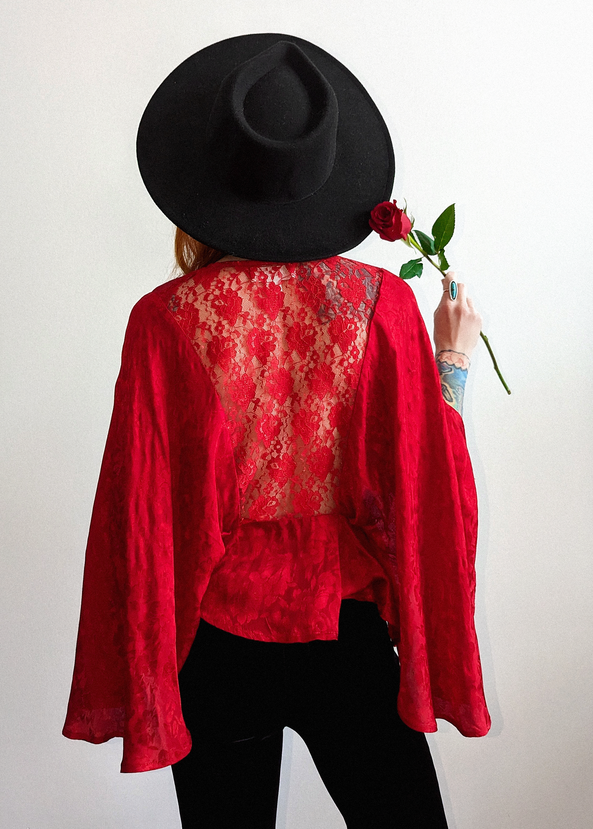70s inspired ruby red satin batwing cape top with deep v-neckline and tonal floral pattern throughout the red satin fabric. Tassel tie details at front and red lace at back