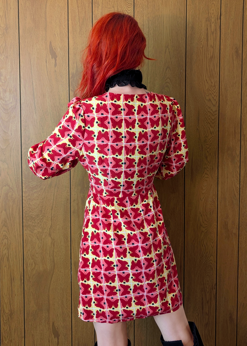 back view of a pink, yellow, and red geometric butterfly mini dress with long sleeves