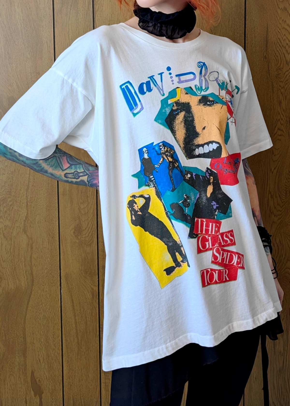Person wearing a white David Bowie t-shirt with colorful graphic design against a wooden panel background