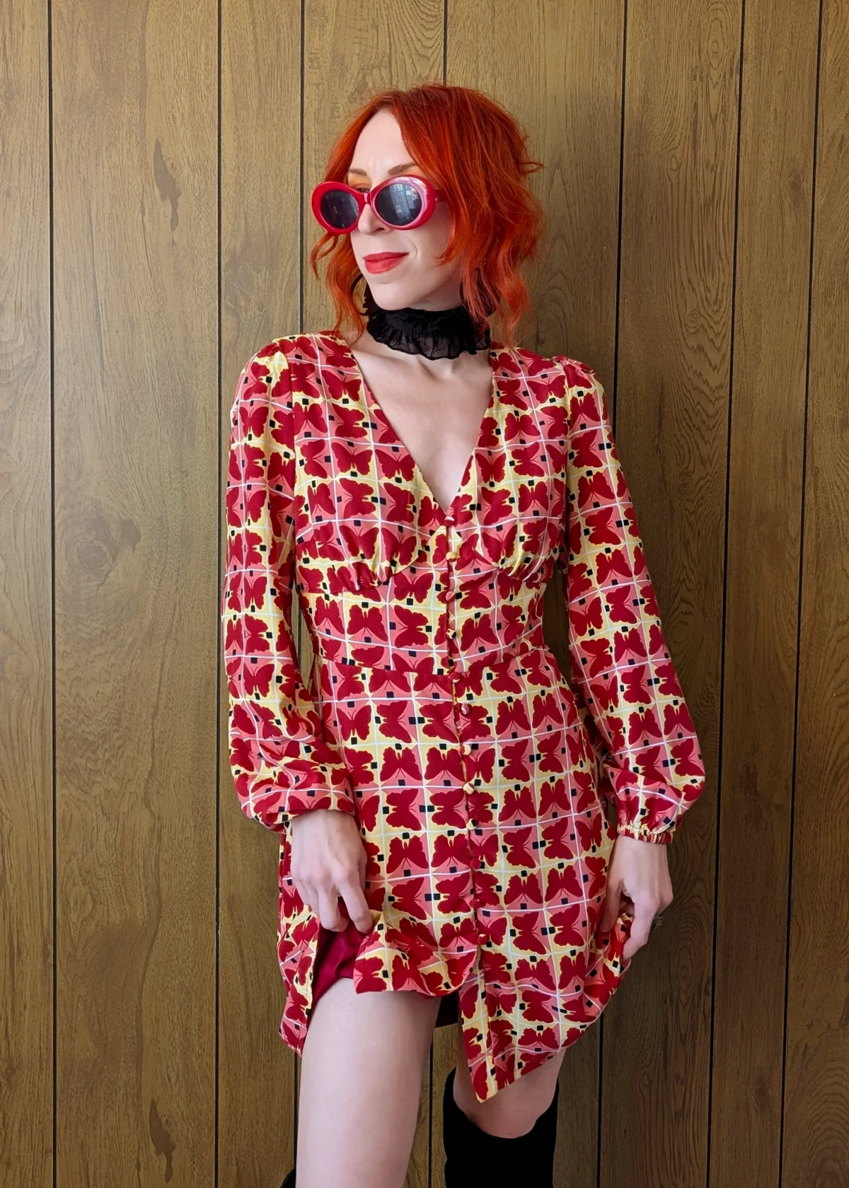 Person wearing a red, pink, and yellow butterfly geometric patterned dress against a wooden panel background