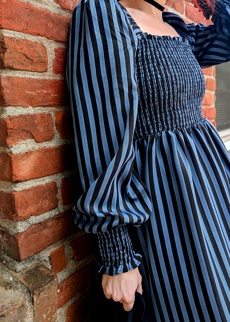 Person wearing a blue and black striped dress against a brick wall.