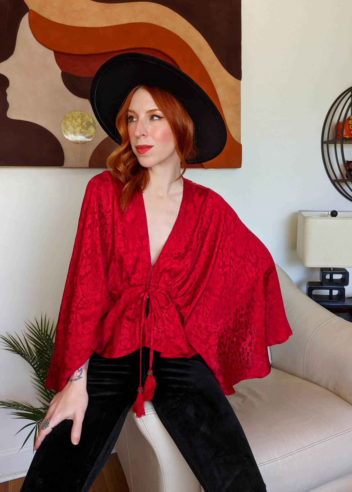 70s inspired ruby red satin batwing cape top with deep v-neckline and tonal floral pattern throughout the red satin fabric. Tassel tie details at front 
