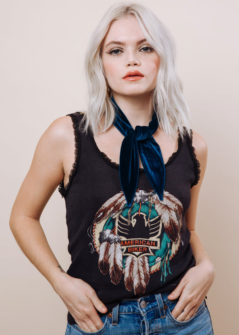 Woman wearing a black graphic tank top and blue scarf, against a plain background