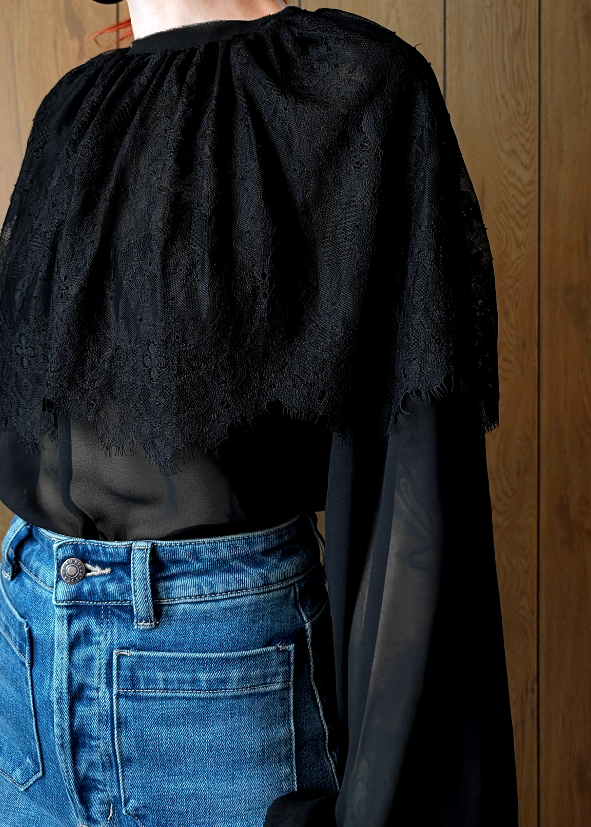 Person wearing a black lace top and blue jeans against a wooden background