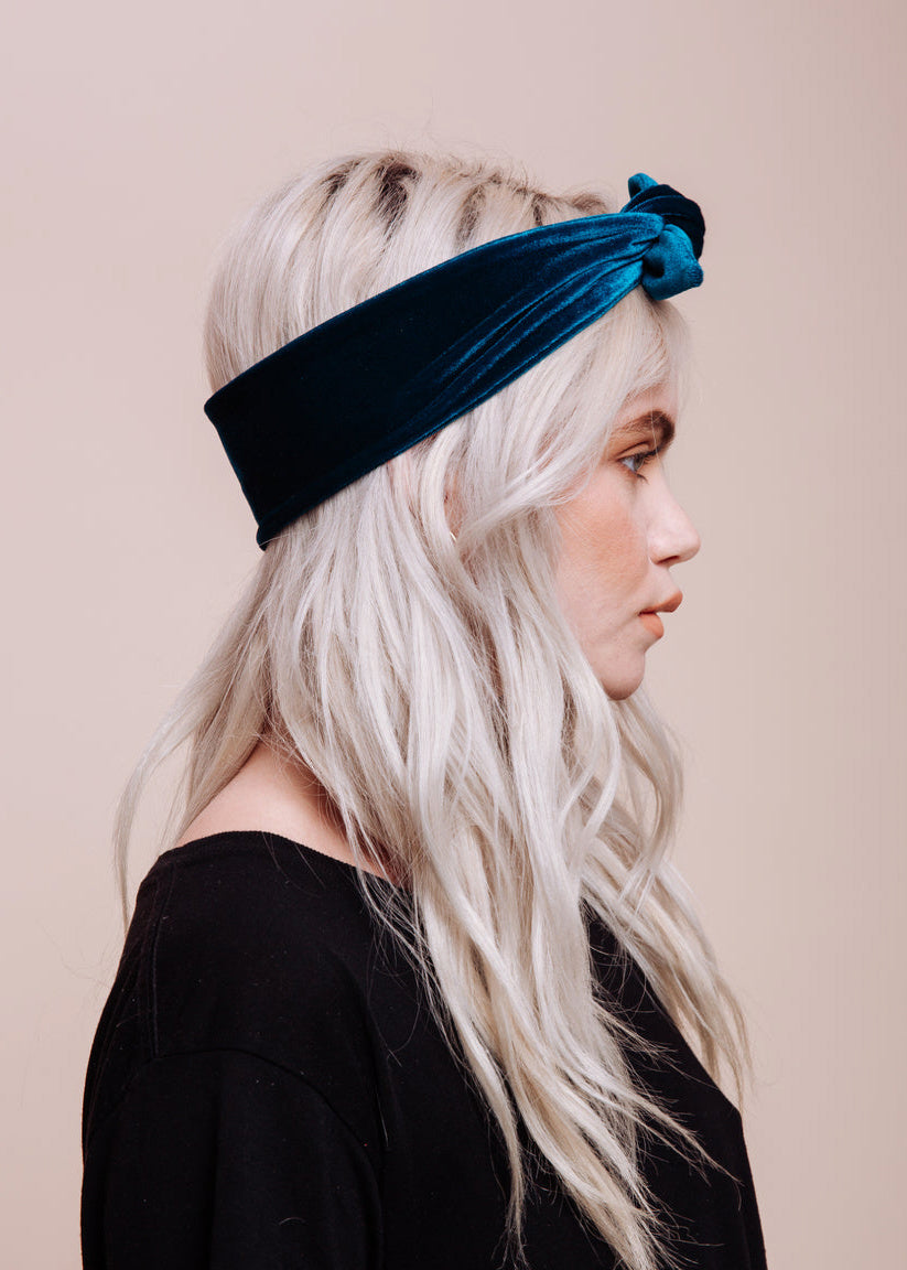 Woman wearing a blue velvet scarf as a headband against a beige background