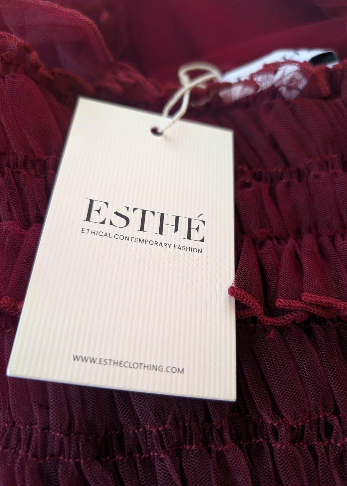 Burgundy tulle fabric with an 'ESTHE' label on a clothing tag
