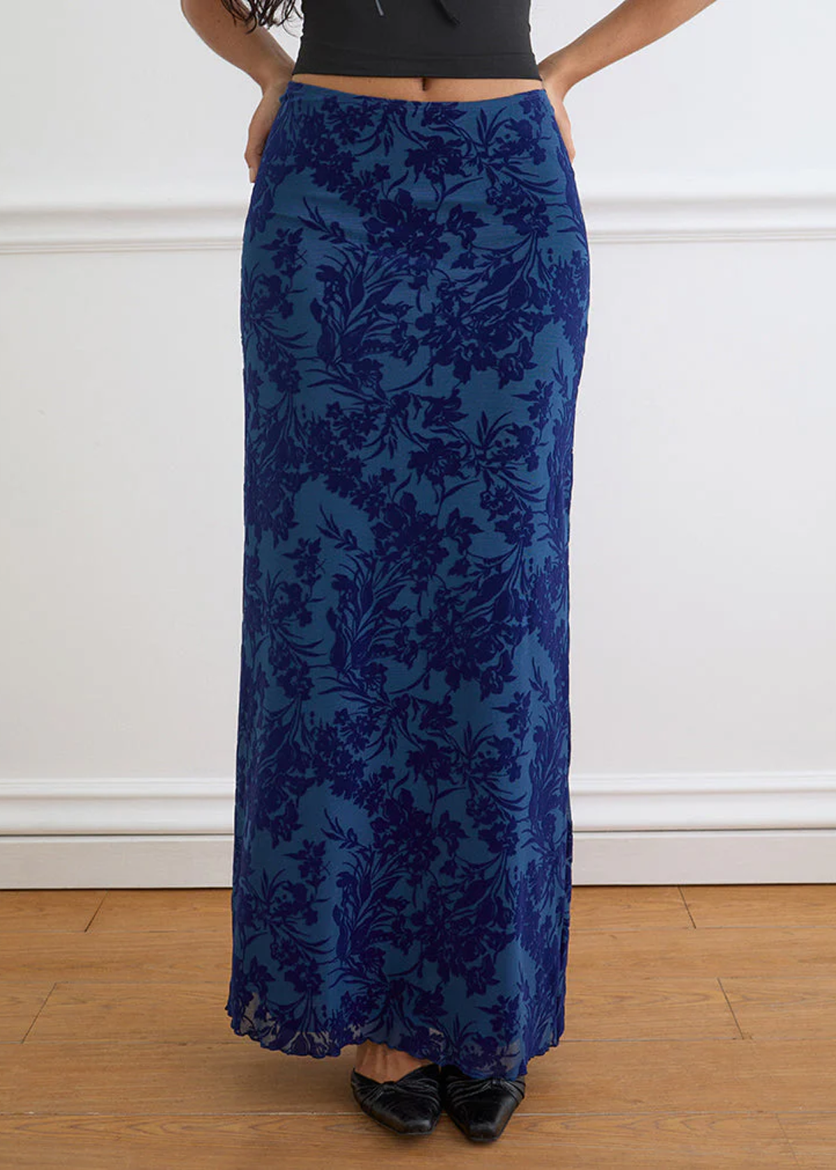 Person wearing a blue floral patterned skirt against a white wall.