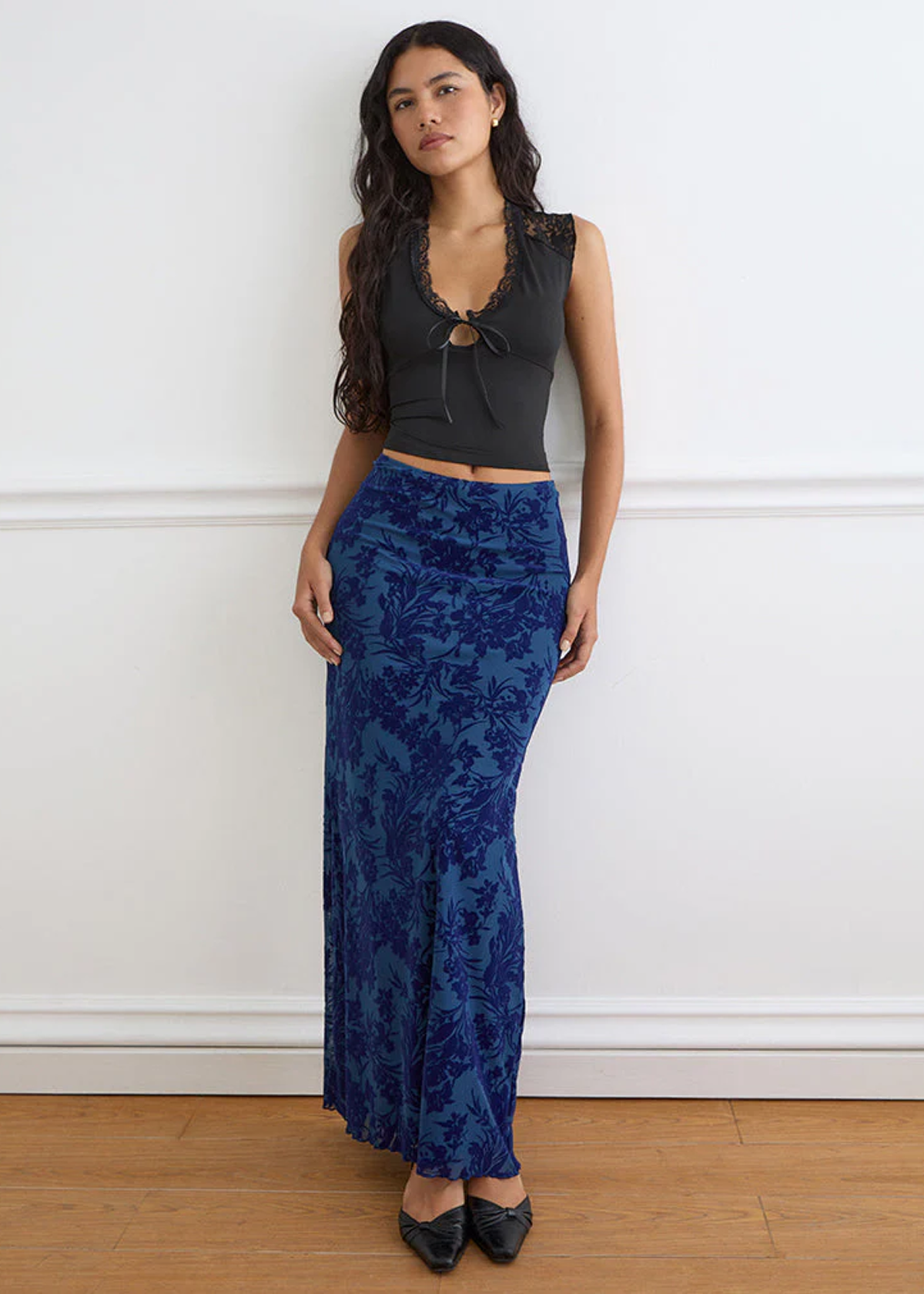 Woman wearing a black top and blue floral pants against a white wall.