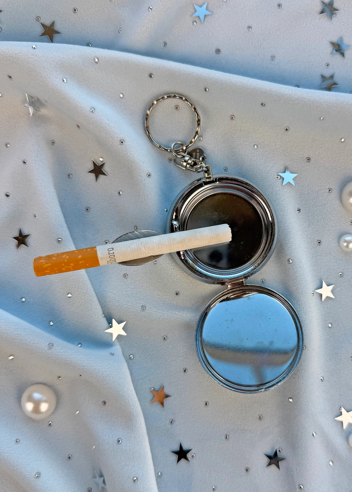 Compact mirror keychain with a cigarette on a star-patterned fabric background