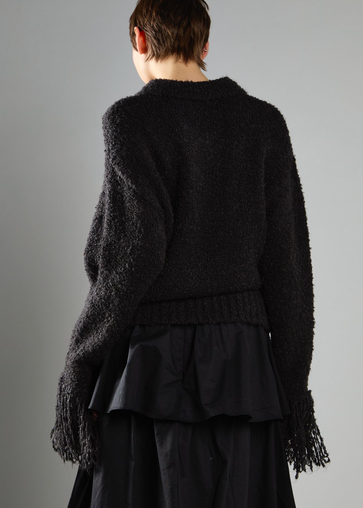 Person wearing a black textured cardigan over a black dress on a gray background