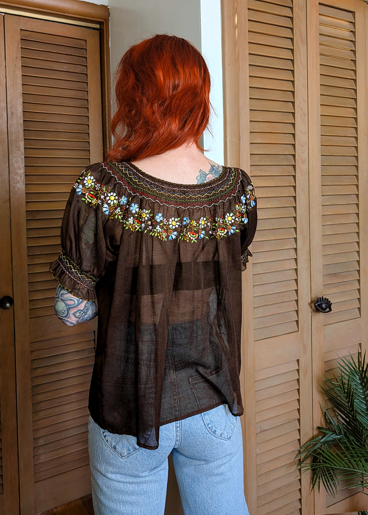 Vintage 1970s gauzy cotton prairie Penny Lane blouse featuring a round neckline, short puff sleeves, and colorful floral embroidery along neckline. Chocolate brown colorway