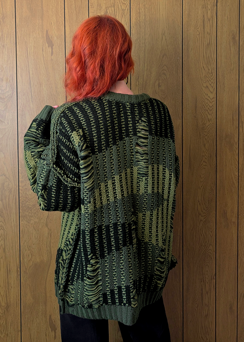 Person wearing a green patterned sweater against a wooden wall