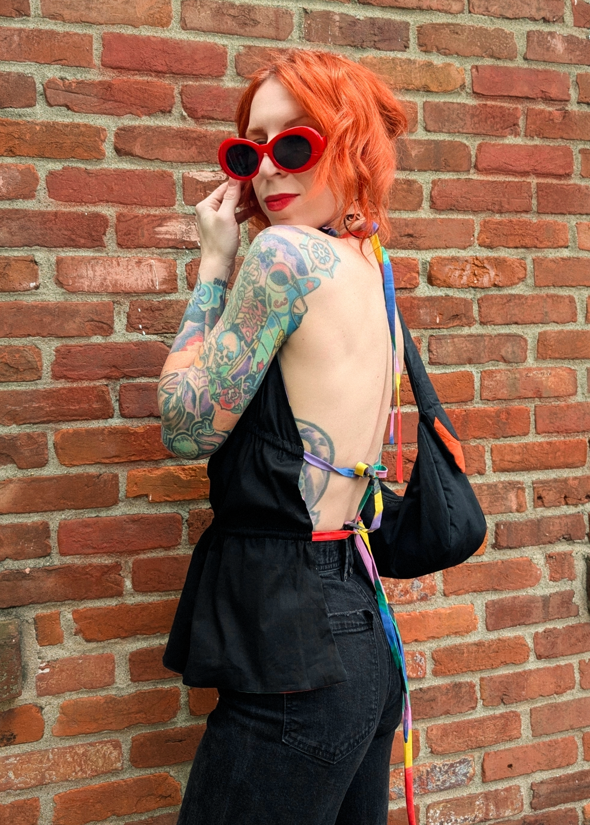 Person with tattoos and colorful hair wearing a black backless halter top with rainbow ties at back