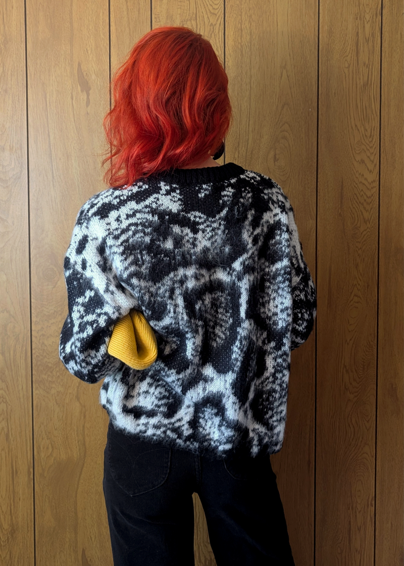back view of a snakeskin print sweater worn by a redheaded woman against a wood paneled backdrop