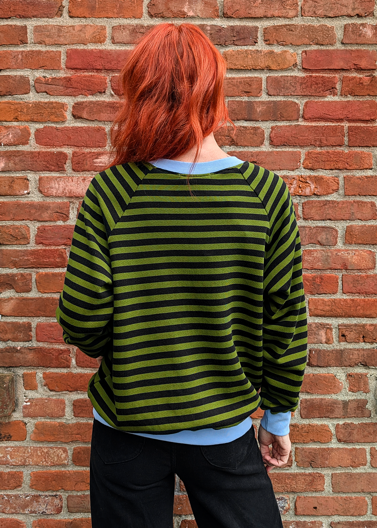 Back view of the Olive green and black stripe raglan crew neck sweatshirt with ribbed sky blue cuffs, collar, and hem. Slouchy, relaxed fit. Made of 100% french Terry cotton