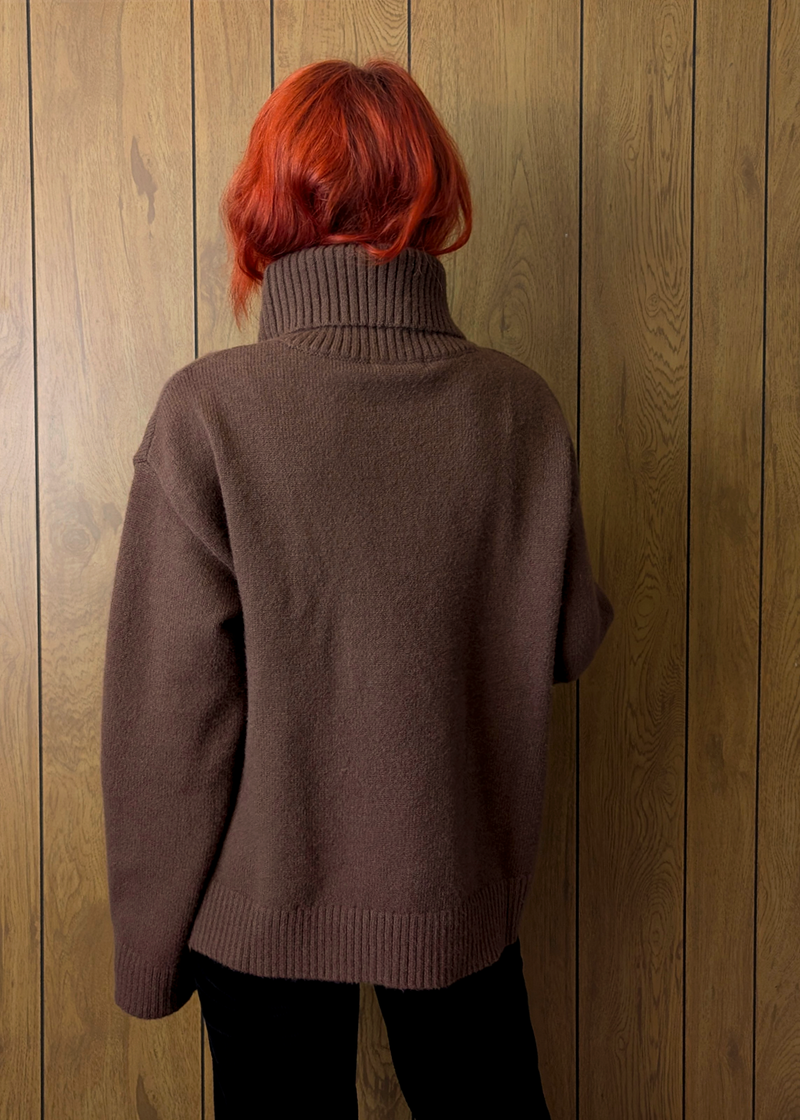 Person wearing a brown sweater against a wooden panel background