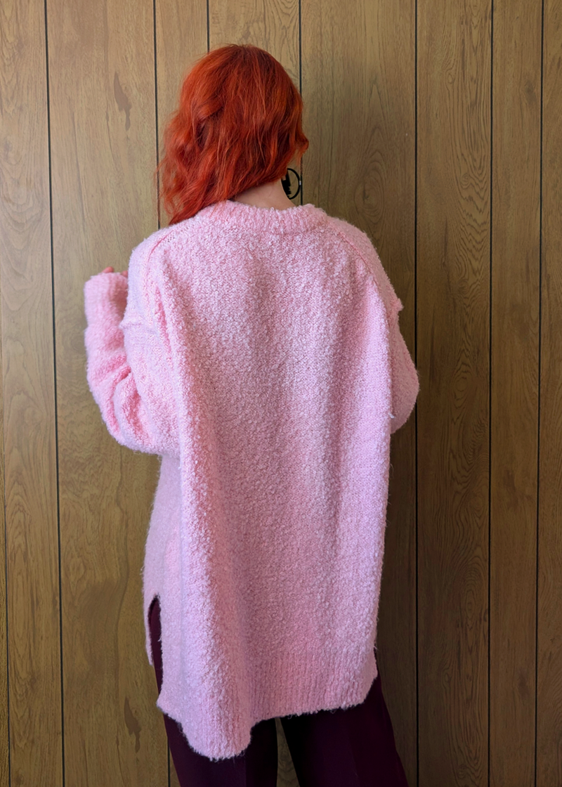 Person wearing a pink fluffy sweater against a wooden wall