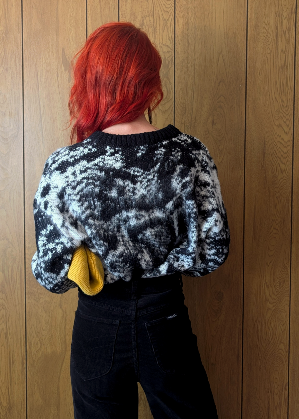 Person wearing a black and white patterned sweater against a wooden wall
