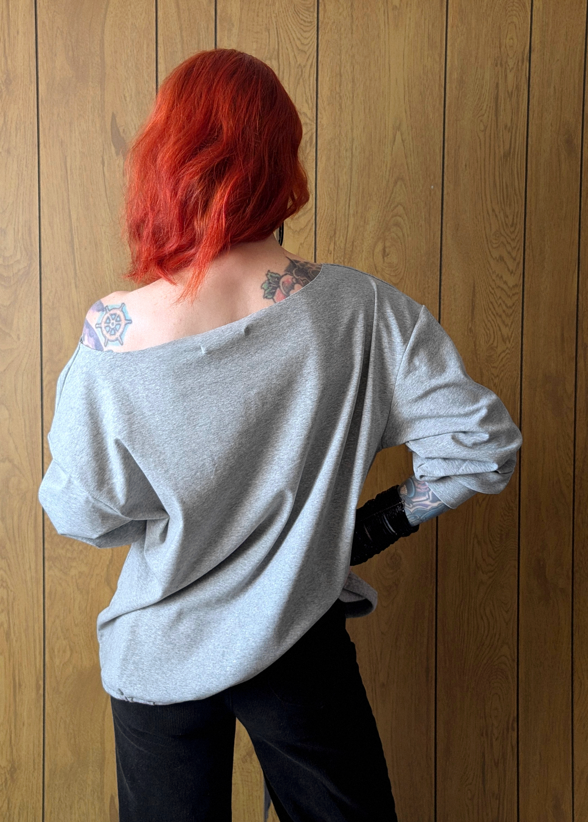 Back view of a woman with red hair wearing a gray jersey against a wooden wall