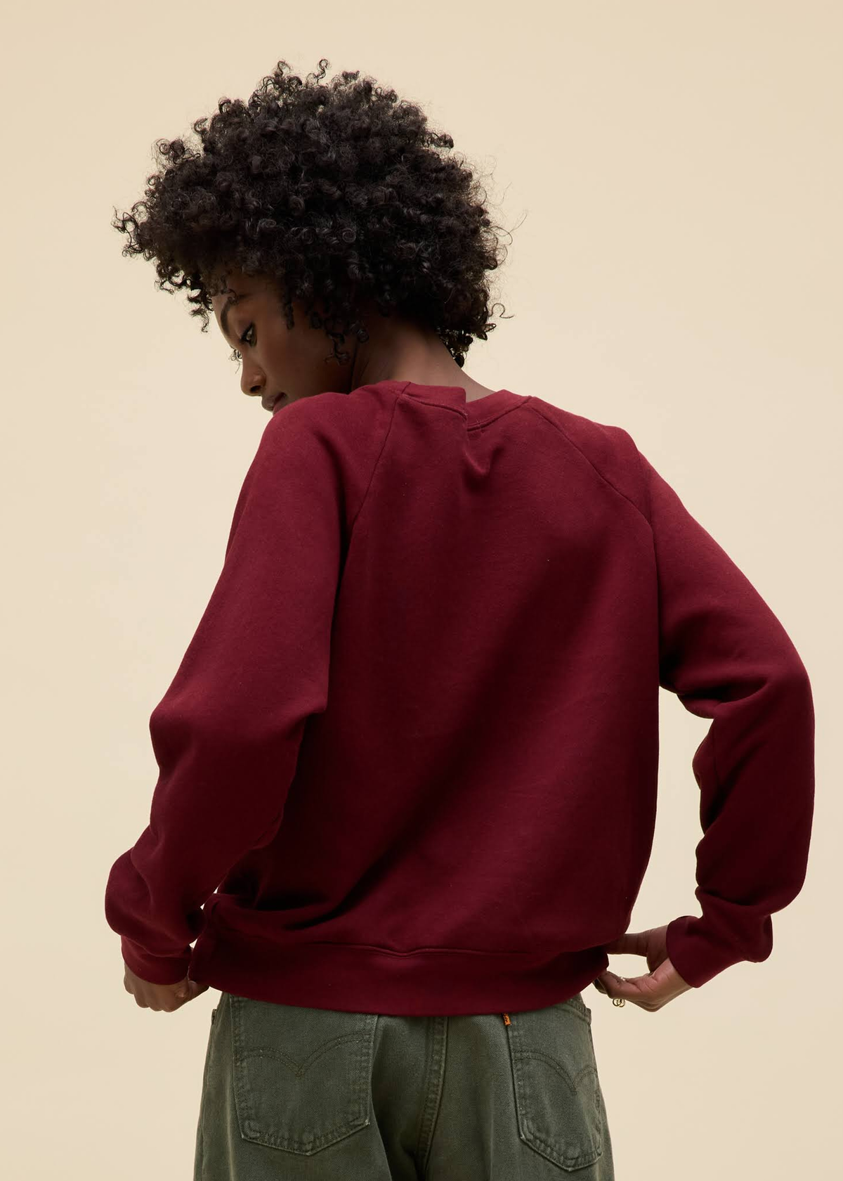 Person wearing a maroon sweatshirt and green pants against a beige background