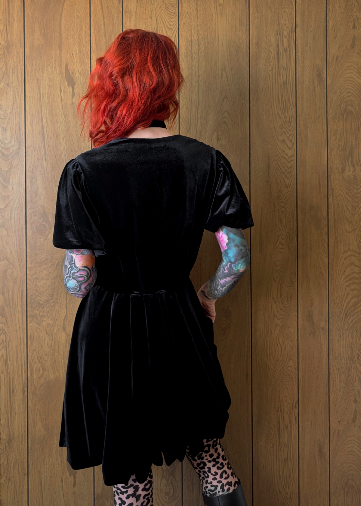 back view of a person wearing a black velvet dress against a wooden wall