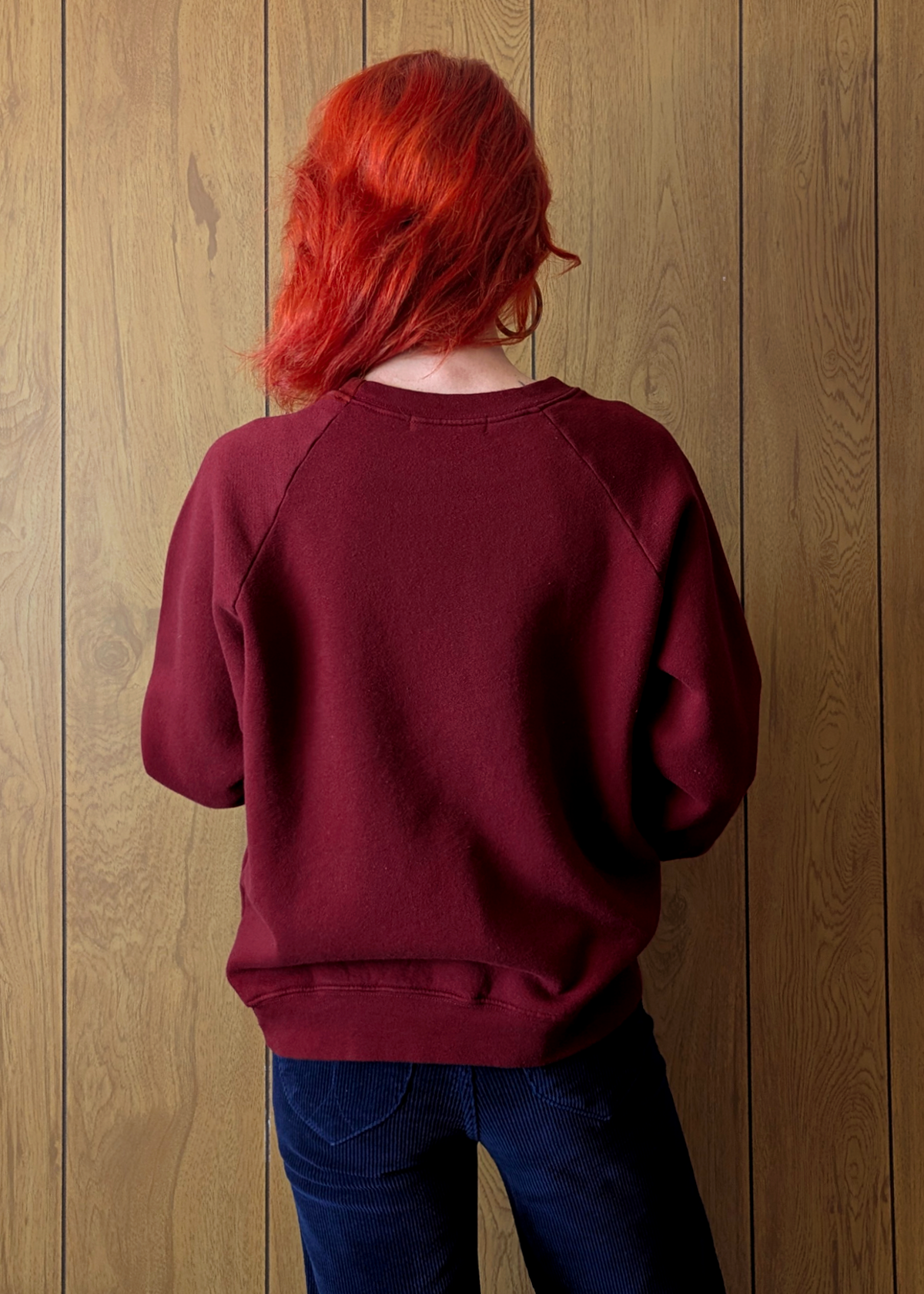 back view of a Person wearing a maroon sweatshirt against a wooden wall