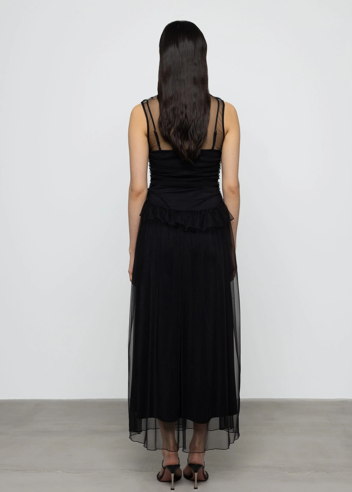 Woman wearing a black dress with sheer overlay against a white background
