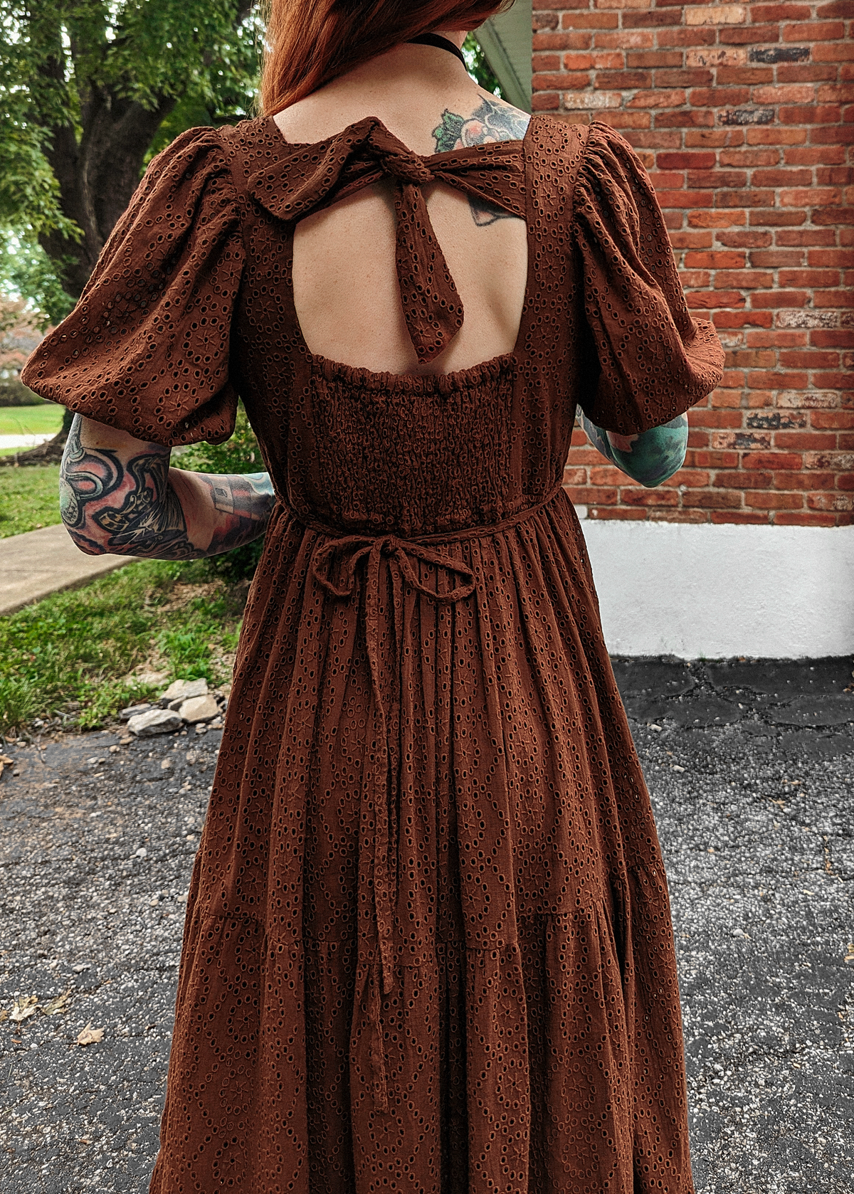 70s inspired prairie dress made of 100% eyelet cotton in a walnut brown colorway. Features puff sleeves, sweetheart neckline, smocked back with tie closure, and ruffled tiered skirt. 