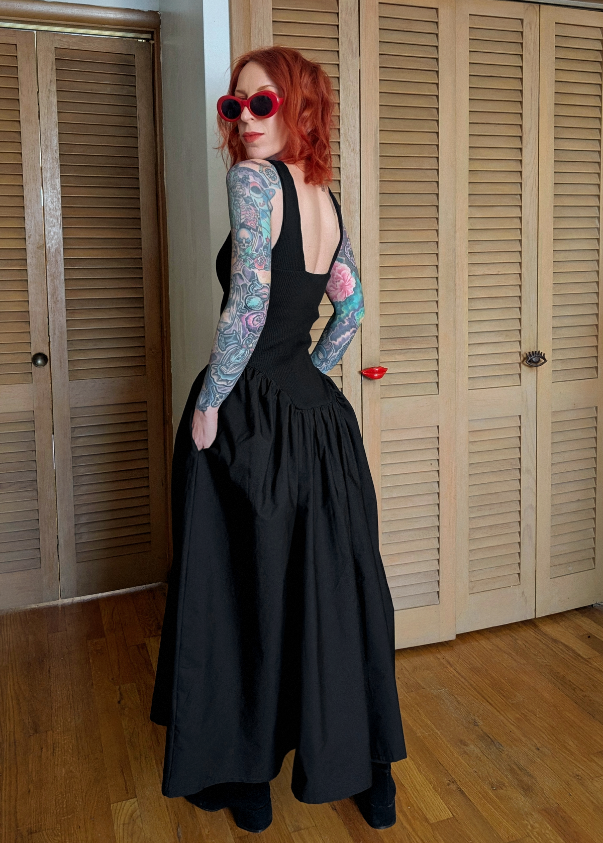 Person wearing a black dress in a room with wooden floors and white walls.