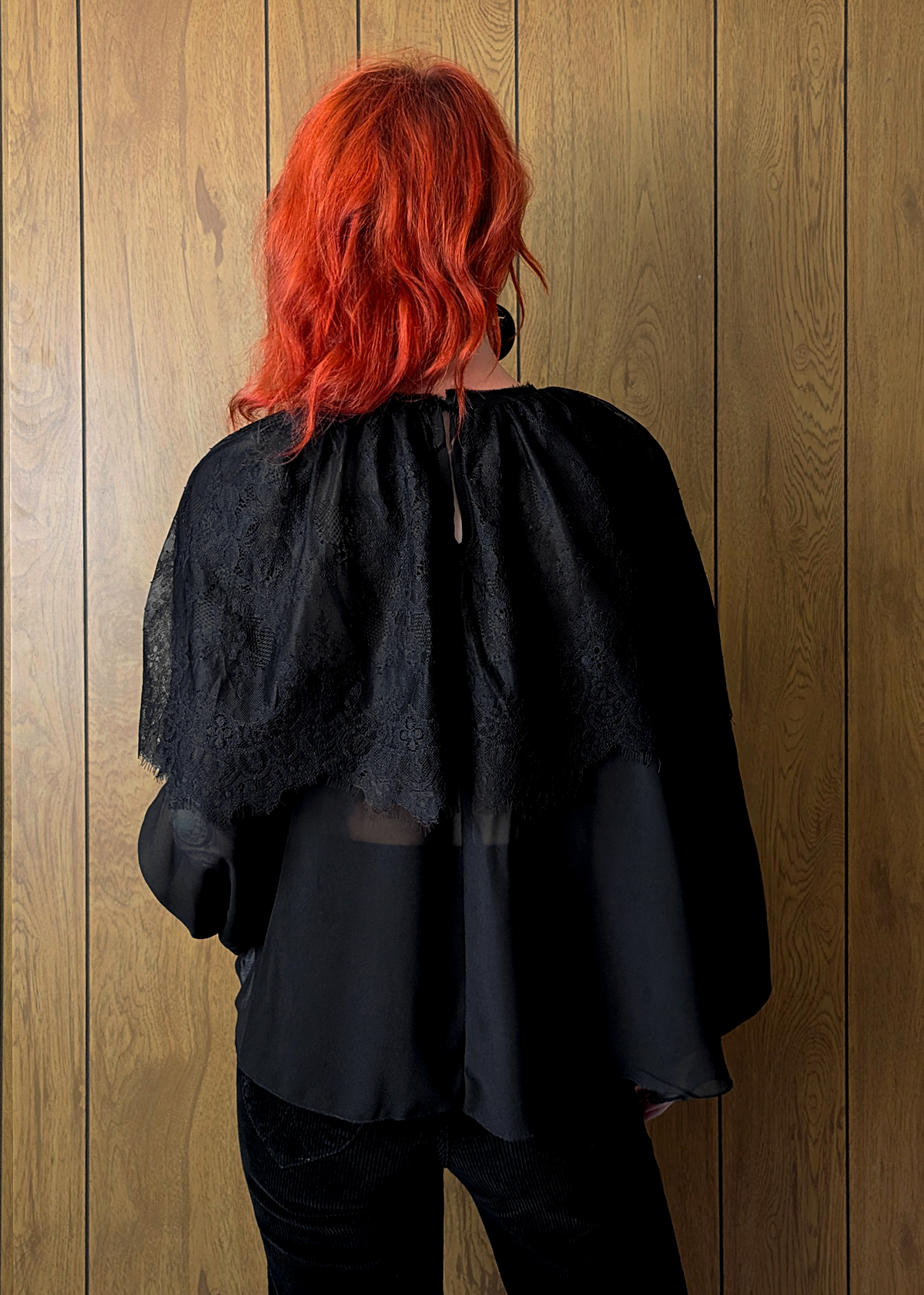 Person with red hair wearing a black lace top against a wooden panel background