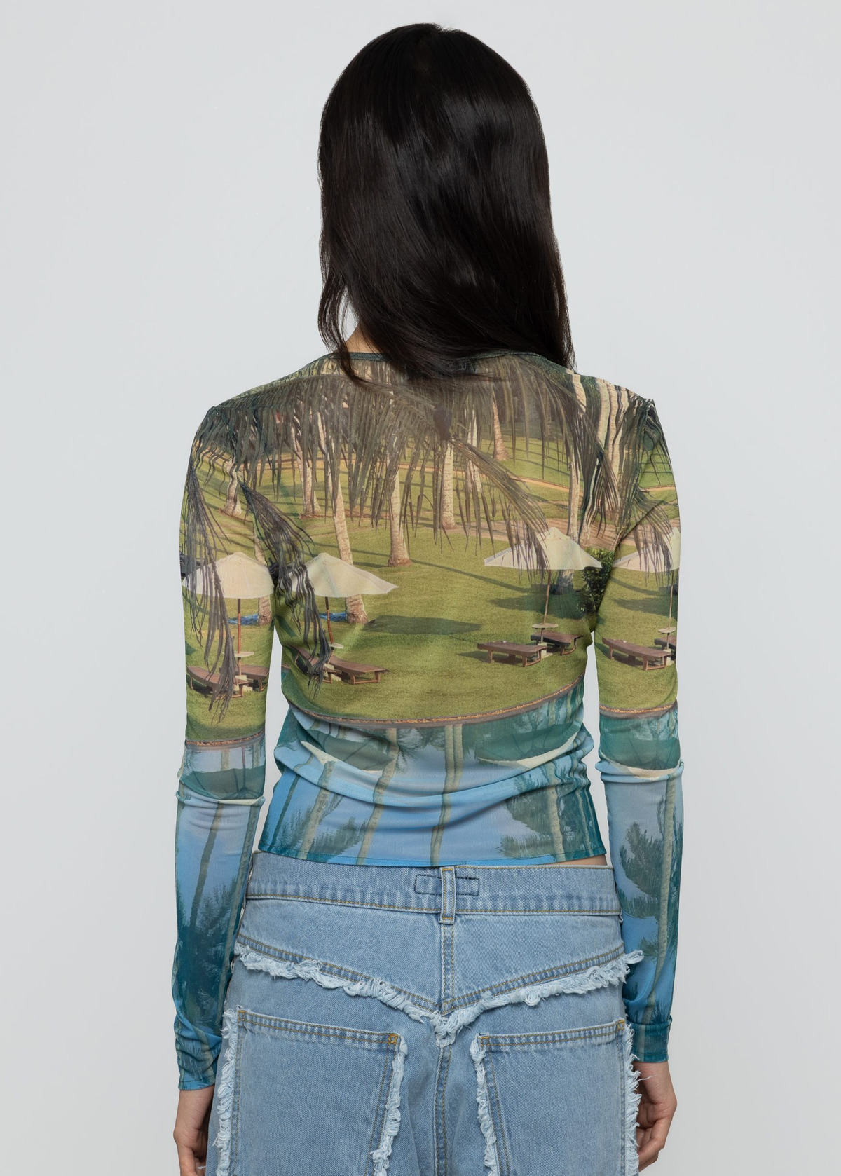 Woman wearing a long-sleeve top with tropical-themed print against a plain background