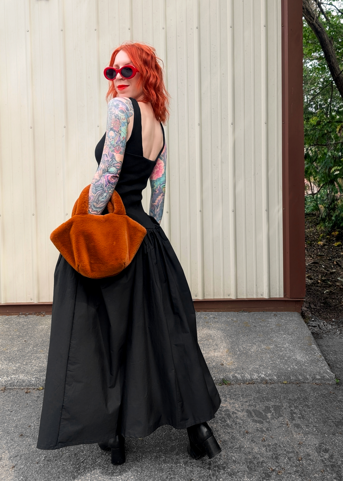 Person wearing a black dress with a large orange bag, standing outdoors.
