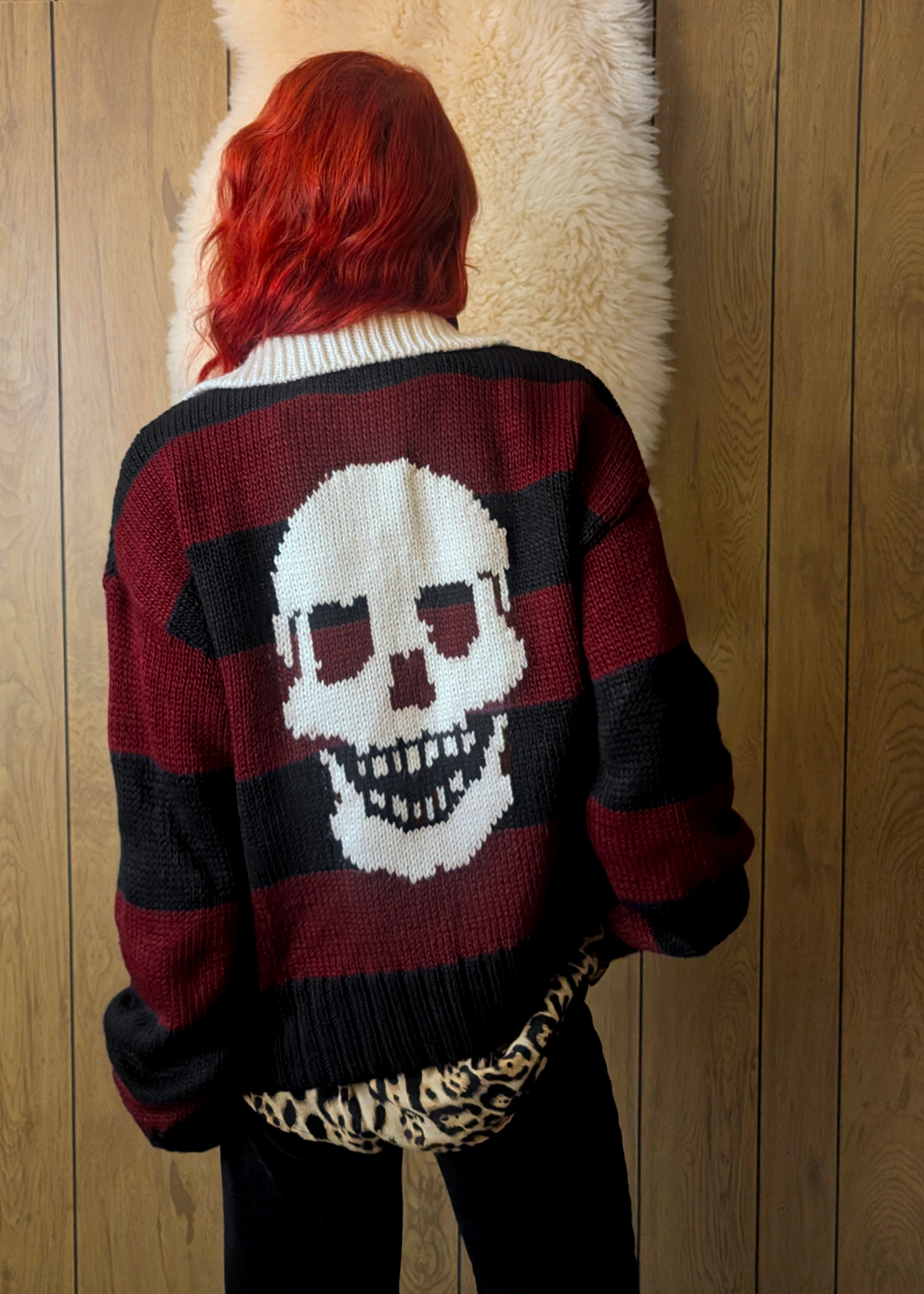 Person wearing a sweater with a skull design against a wooden wall.