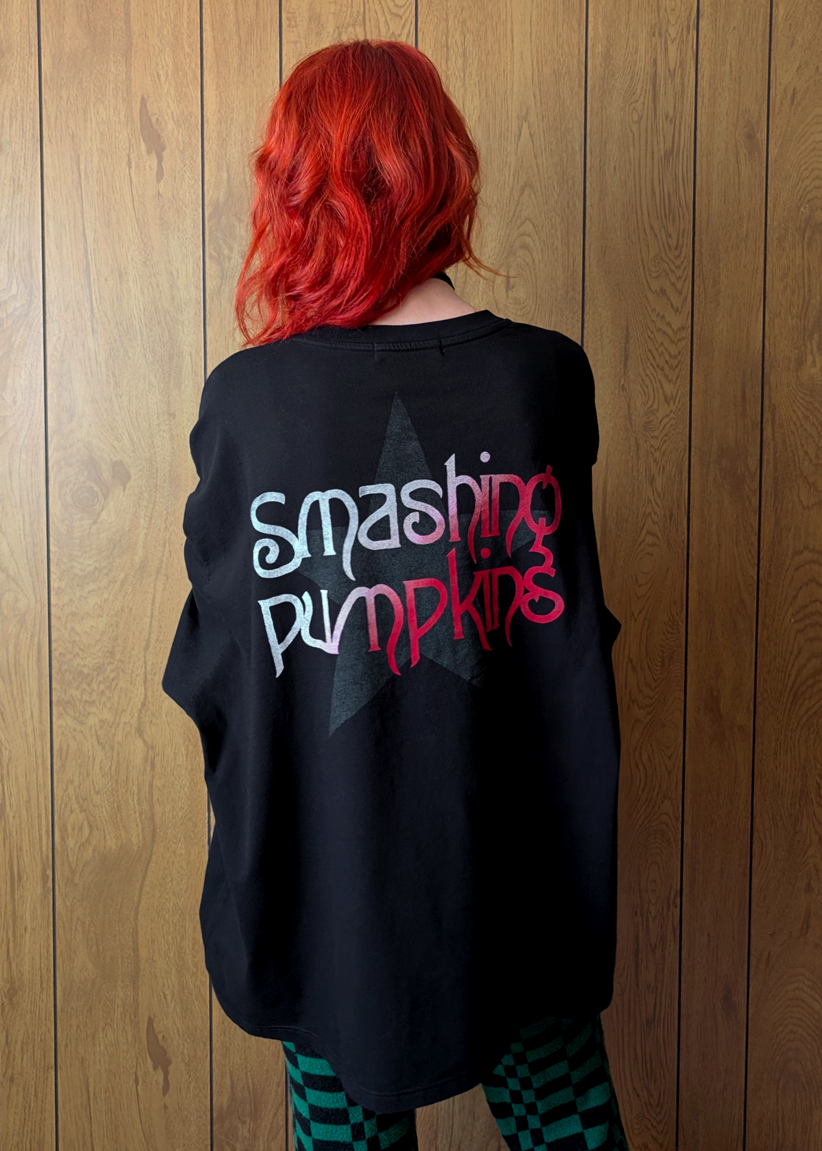 Person wearing a black long sleeve shirt with 'Smashing Pumpkins' text against a wooden panel background