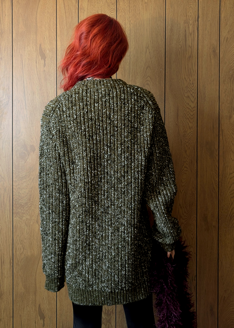 Person wearing a textured green sweater against a wooden panel background