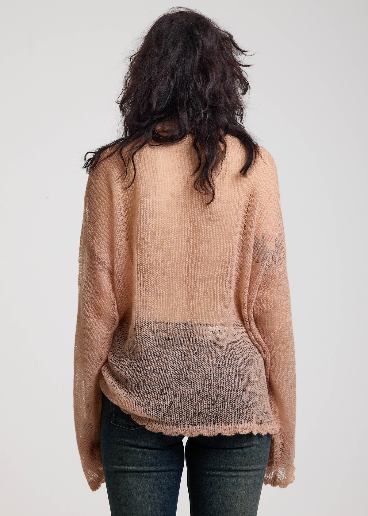 Back view of a woman wearing a dusty pink open knit lightweight sweater on a plain background