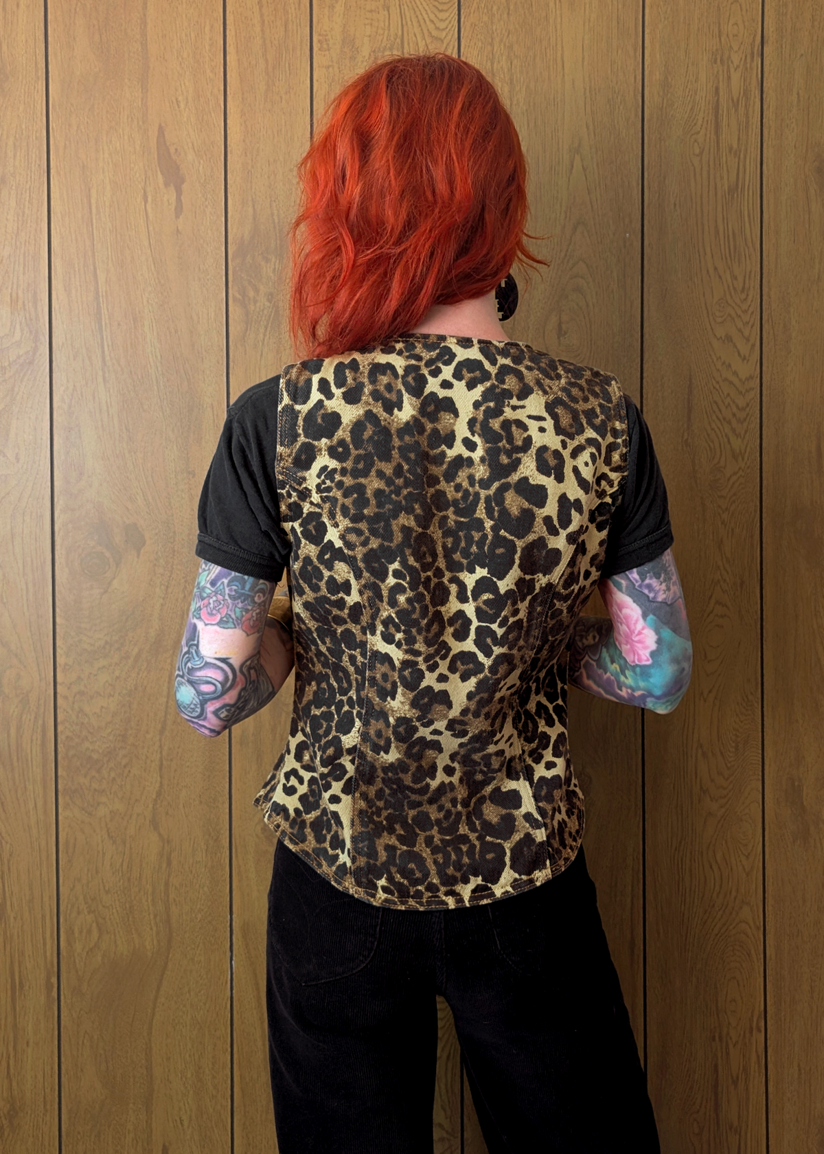 Person wearing a leopard print vest against a wooden wall