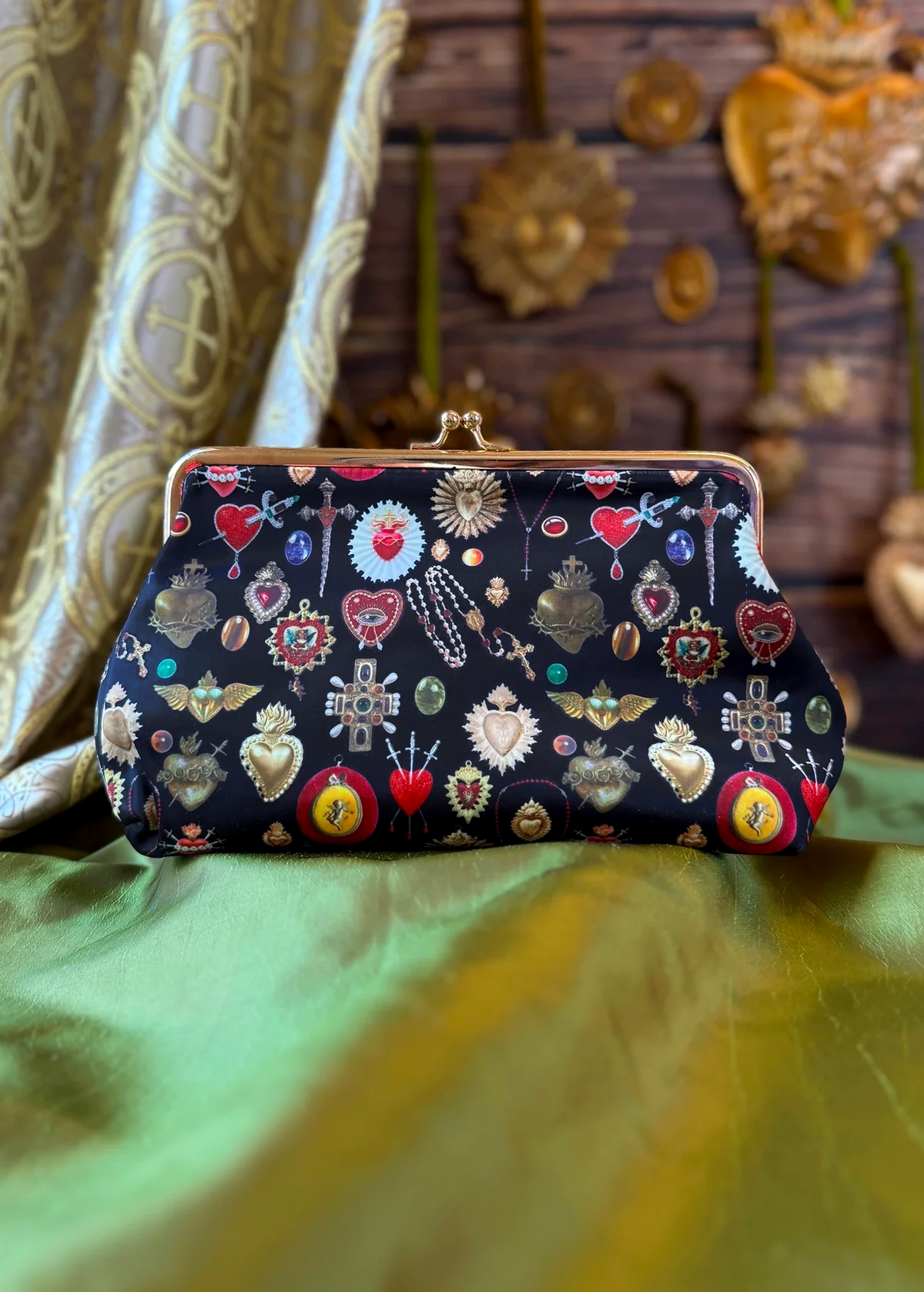 Black clutch bag with decorative heart and star pattern sitting against a green fabric backdrop