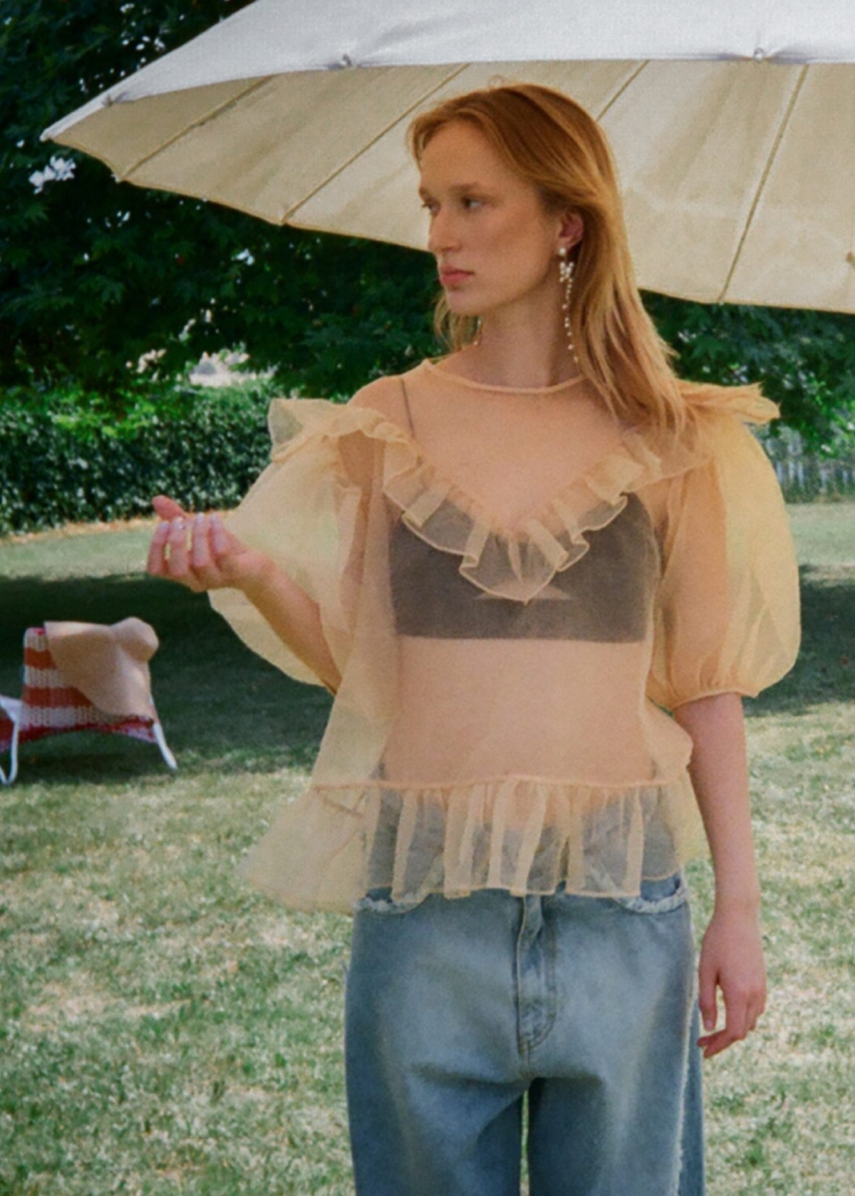 Woman wearing a voluminous sheer organza top with puffed sleeves outdoors under an umbrella