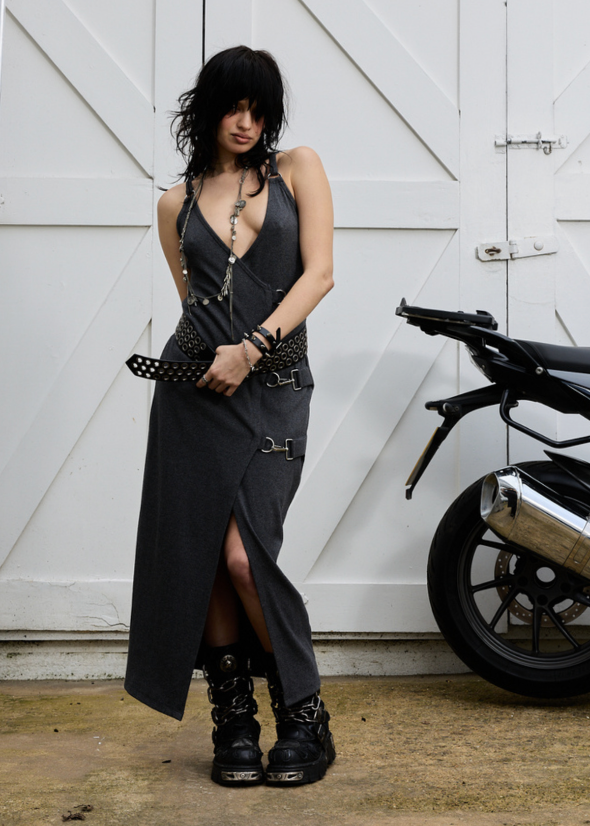 Woman in a charcoal grey ribbed tank dress standing next to a motorcycle in front of white wooden doors.