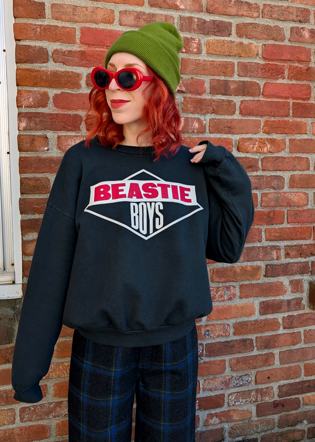 Person wearing a black sweatshirt with 'Beastie Boys' logo in front of a brick wall