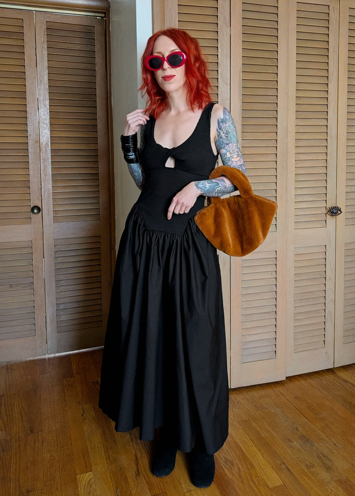 Woman in a black dress holding a rust faux fur bag against wooden shutters.