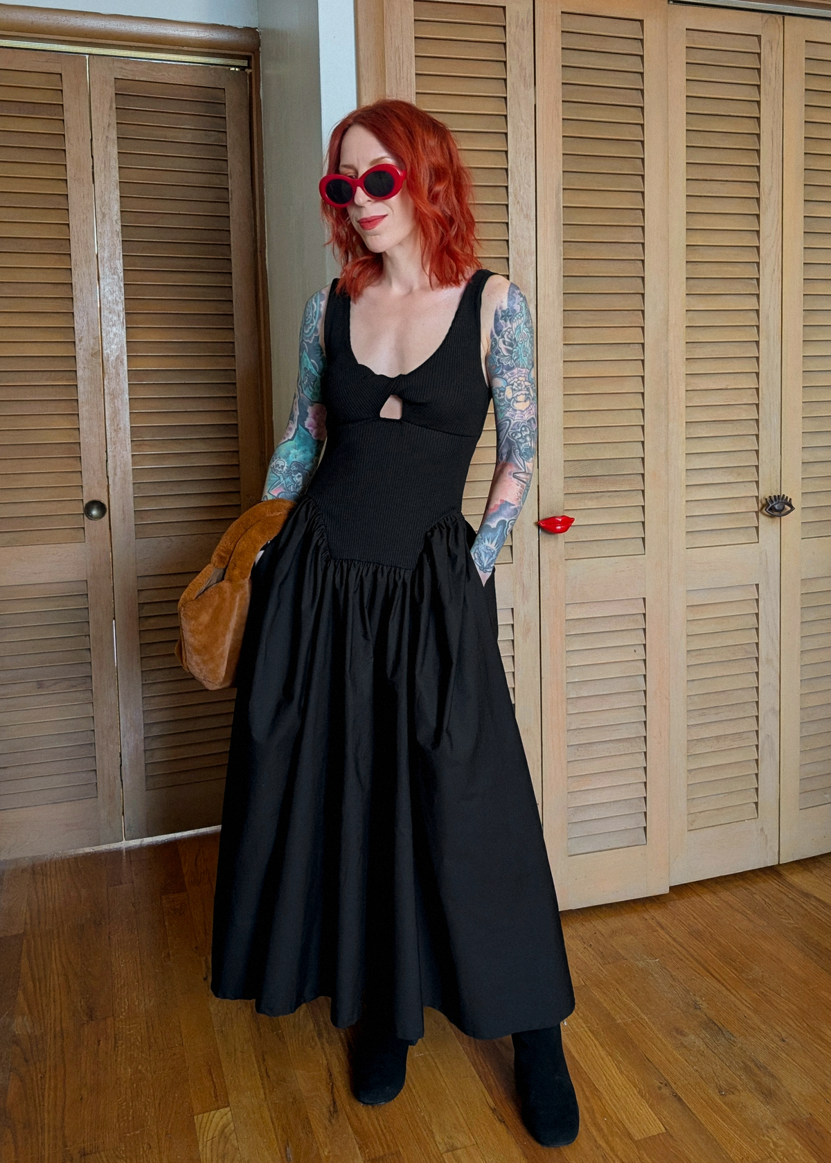 Woman with red hair wearing a black dress standing in front of wooden doors.
