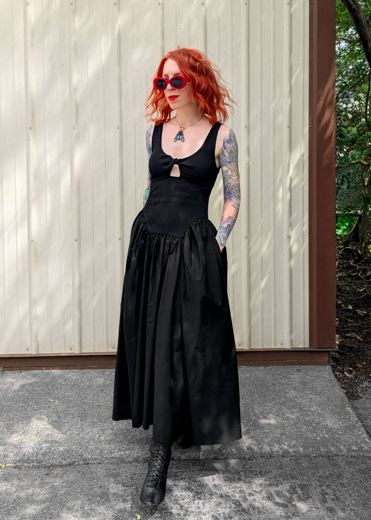 Person wearing a black dress with a wooden fence and greenery in the background