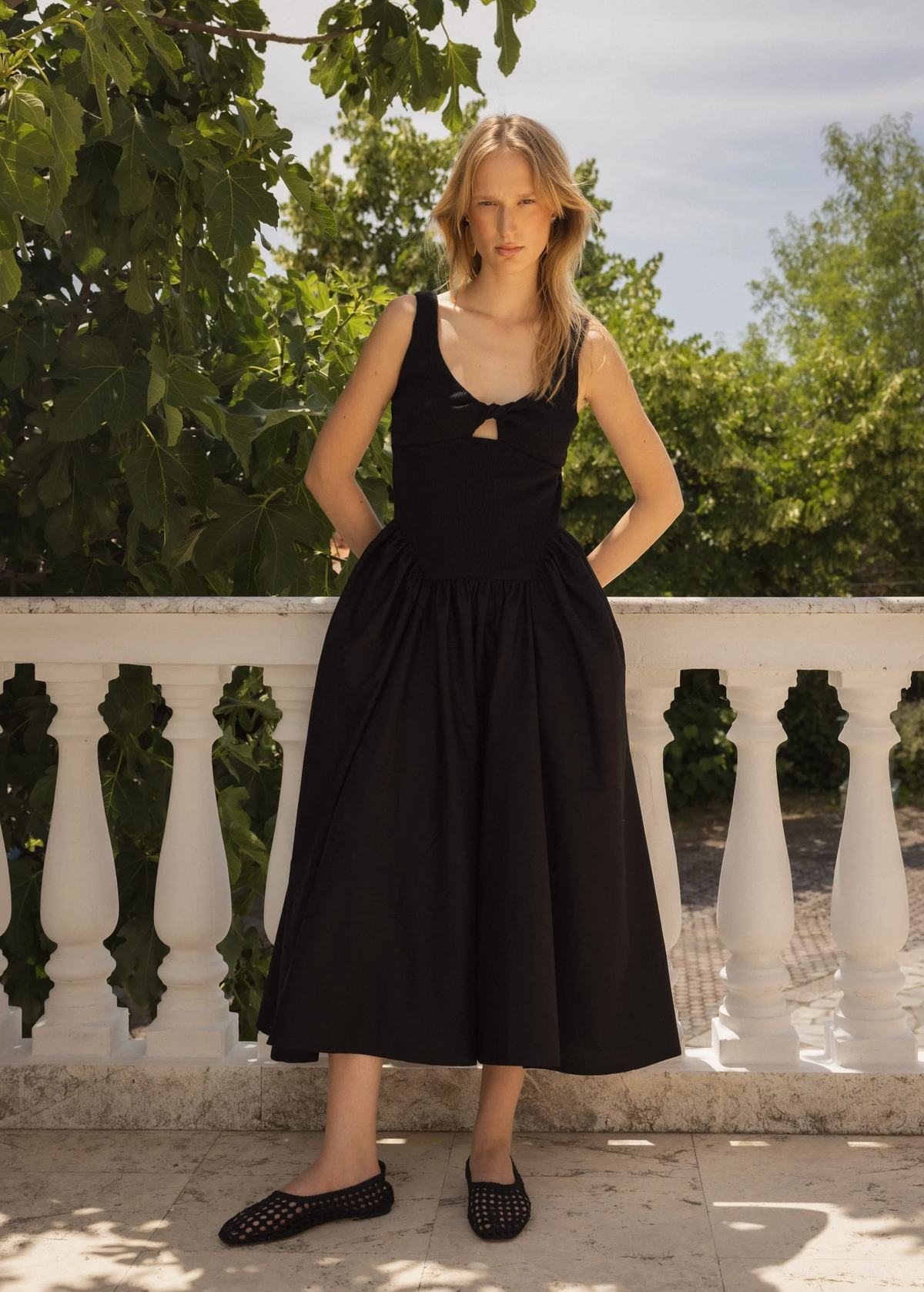 Woman wearing a black dress standing on a balcony with greenery in the background