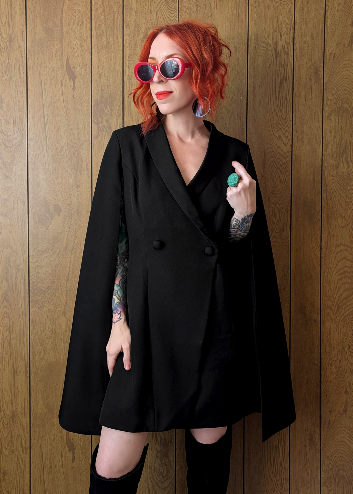 Person wearing a black blazer cape dress and sunglasses against a wooden background