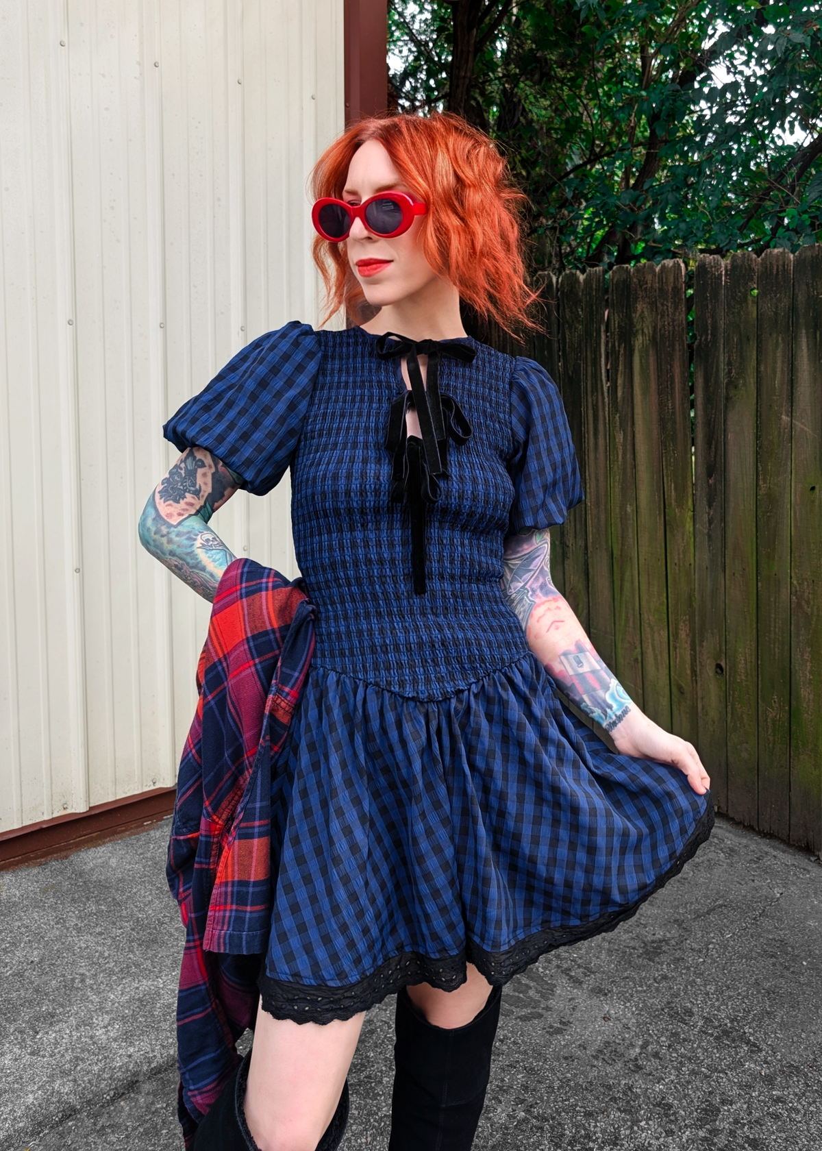 Person wearing a blue and black checkered dress with a plaid flannel in hand, standing outdoors.