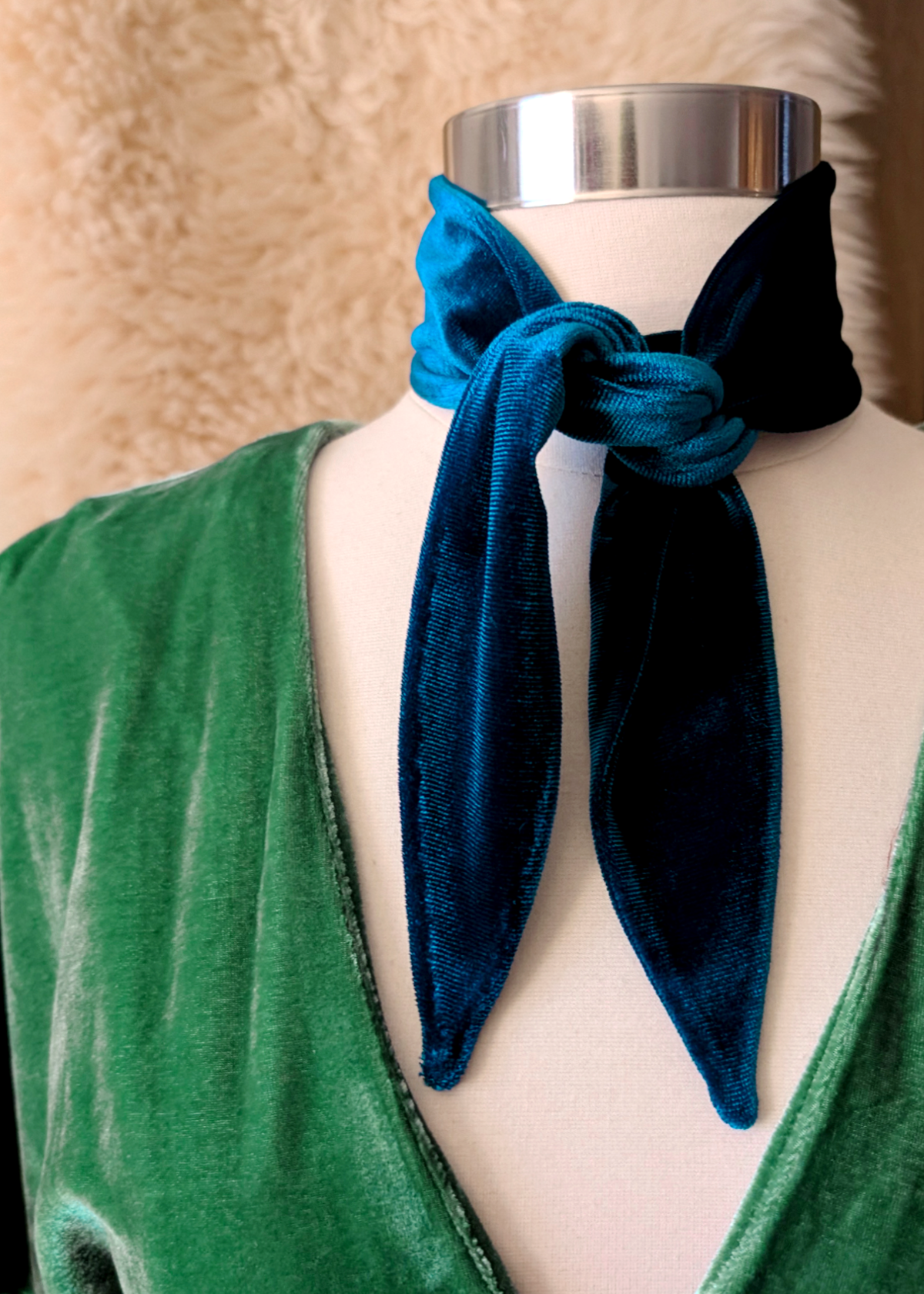 Mannequin wearing a green dress with a blue velvet scarf tied around its neck against a beige background