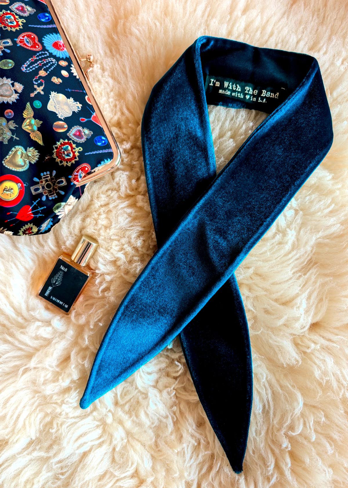 Blue scarf with a label, perfume bottle, and colorful case on a fluffy beige surface