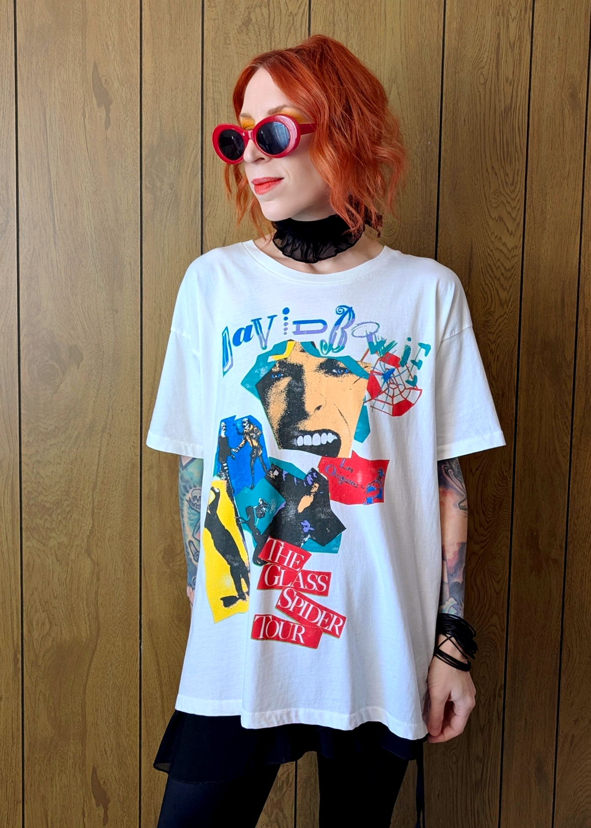 Person wearing a David Bowie Glass Spider Tour graphic t-shirt with colorful design against a wooden panel background